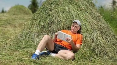 穿着带有平板电脑的橙色t恤的男人坐在干草堆附近