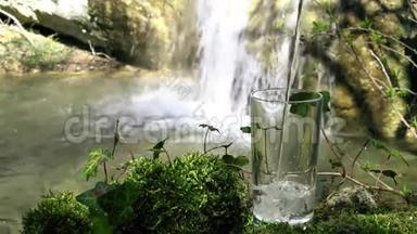 玻璃饮用天然水与瀑布在柔和的焦点背景。 从泉水中流出的纯净生态水