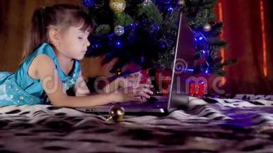 圣诞<strong>树下</strong>有笔记本电脑的女孩。 在新年里，孩子在一棵<strong>树下</strong>，手提电脑。 一个小女孩