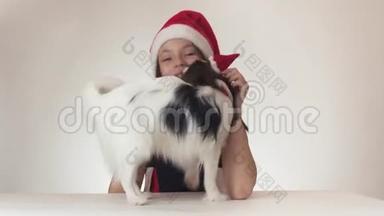 美丽的少女和狗大陆玩具斯帕尼尔·帕皮隆戴着圣诞老人的帽子，快<strong>乐</strong>地亲吻和<strong>愚</strong>弄着