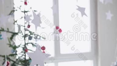 纸星星挂在窗户旁边的一棵圣诞树的背景上。 圣诞节的概念。 慢动作。 4k