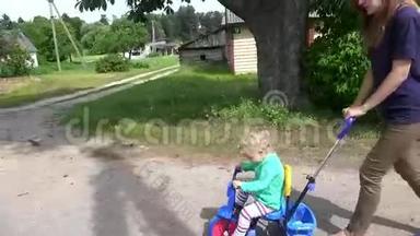 年轻的母亲推着金发蹒跚学步的女孩骑着小三轮车。