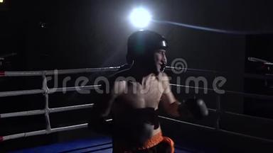 两个戴着头盔和拳击手套的人在黑暗中在擂台上战斗。 慢动作