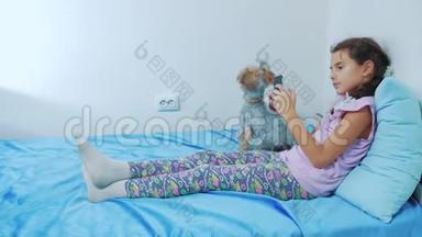 <strong>可爱</strong>的女孩<strong>和狗</strong>宠物躺在床上的智能手机肖像。 小女孩<strong>和狗</strong>宠物玩网络游戏