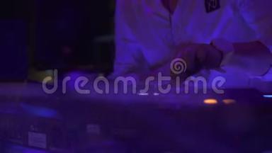 男D J在舞蹈俱乐部的派对上在音响控制台播放家庭音乐。 混合音乐和彩色光线的DJ控制器