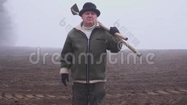 戴着帽子的高级农民，手里拿着一把泥泞的<strong>锄头</strong>和田野上的草叉。 体力劳动。 福克