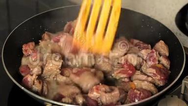 在煎锅里煎肉。 煎锅里的肉与木铲混合。 肉在自己的果汁中沸腾