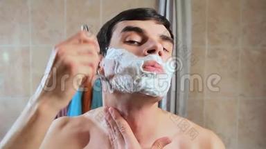 一个人用剃<strong>刀</strong>在泡沫中剃了他的脸。 他在镜子前<strong>刮胡子</strong>