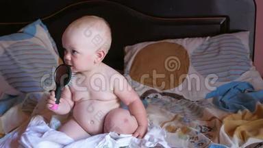 漂亮的宝宝在床上玩梳子。 微笑并试图梳理自己。 孩子一年。 梳子上有一面镜子