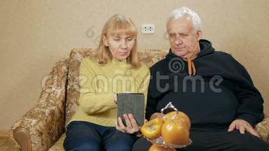 一对老夫妇手持数码平板电脑、坐在客厅沙发上微笑的画像