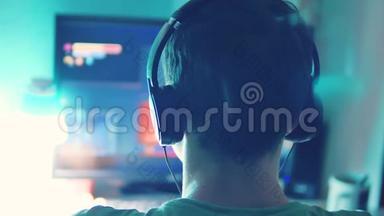 青少年男孩通过耳机中的网络监视器在电脑上玩网络游戏。 青少年男子玩电子游戏的生活方式在