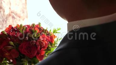 有花的房间。 穿着夹克和白衬衫的人手里捧着一束美丽的红玫瑰。 特写镜头。 美丽美丽