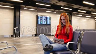 年轻漂亮的红头发和眼镜的女人在机场<strong>候机</strong>厅使用小玩意