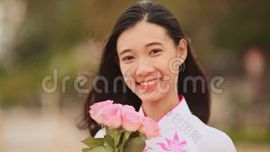 越南女孩穿着民族服装和服装，为相机摆姿势和微笑。 手里拿着粉红色