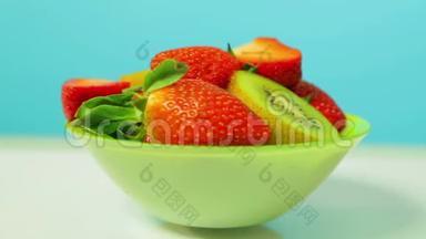 绿色盘子上蓝色背景的鲜奇异果和草莓片旋转成一个圆圈