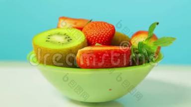 绿色盘子上蓝色背景的鲜奇异果和草莓片旋转成一个圆圈