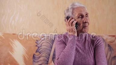 一位坐在沙发上用手机说话的老年妇女。 他通过手机、智能手机进行交流。