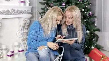两位金发女郎坐在圣诞树附近的地毯上看着平板电脑