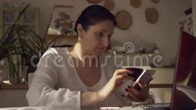 年轻的女设计师正在测试智能手机和电脑上的用户界面。 那个女人看电话。 女人坐着