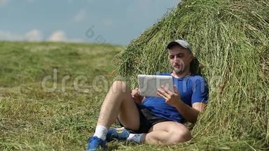 穿着深蓝色t恤的人坐在干草堆附近，通过平板电脑进行交流