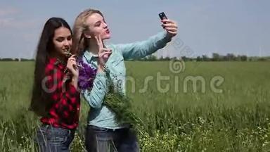 两个年轻女孩带着一束花在绿色的田野上，制作自<strong>拍手</strong>机。