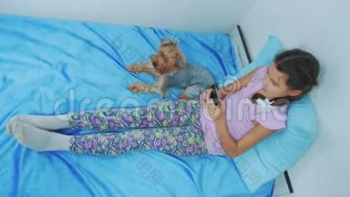 <strong>可爱</strong>的女孩<strong>和狗</strong>宠物躺在床上的智能手机肖像。 小女孩<strong>和狗</strong>宠物玩网络游戏
