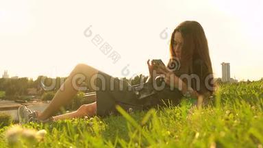 美丽的黑发女孩穿着黑色连衣裙，在<strong>草坪</strong>上使用她的智能手机。 休闲时间。 4K<strong>视频</strong>
