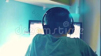 青少年男孩通过耳机中的网络监视器在电脑上玩网络游戏。 青少年男子晚上玩电子游戏