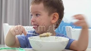 小可爱的孩子坐在<strong>一</strong>张桌子旁，吃自己的燕麦片，孩子吃<strong>得</strong>很自<strong>愿</strong>。 快乐童年的概念。