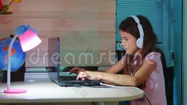 小女孩带着耳机在笔记本电脑上玩网络游戏。 电脑上的小女孩在社交媒体上留言