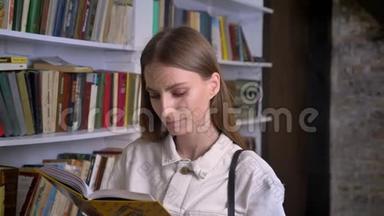 年轻可爱的女孩正在<strong>看书</strong>，在镜头前看，在后台看<strong>图书馆</strong>