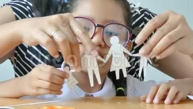 穿着泰国<strong>幼儿园</strong>学生制服的近镜头亚洲小女孩和她的母亲在玩一张白纸，做成家庭形状