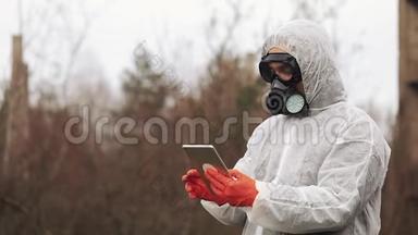 穿着生物危险服和防毒面具的人在被污染的土地上的平板电脑上记笔记