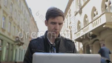 年轻人把手提电脑放在街凳上，微笑着用智能手机说话