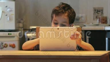 可爱的小孩手里拿着一台白色平板电脑在家里的一张桌子上。 休闲服装