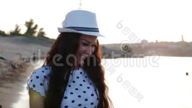 快乐的女孩戴着一顶白色可爱的帽子沿着海边散步，在沙滩上，看着夕阳，微笑着