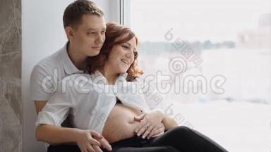 漂亮的怀孕少女坐在窗边。 特点是一只手朝窗户和微笑。 慢动作