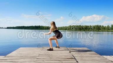 美丽的，运动的年轻金发女人伸展，做不同的运动，<strong>跳跃</strong>，<strong>跳跃</strong>，蹲。 湖泊，河流，蓝色
