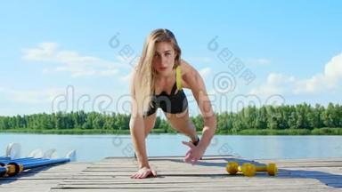 美丽的，运动的年轻金发女人伸展，做不同的运动，<strong>跳跃</strong>，<strong>跳跃</strong>，蹲。 湖泊，河流，蓝色