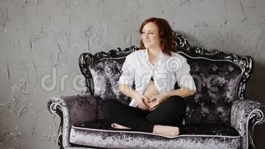 漂亮的红发孕妇。 坐在<strong>老式沙发</strong>上笑。 慢动作