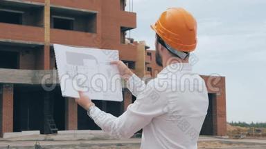 施工现场总建筑师.. 总建筑师戴着安全帽在施工现场看方案，蓝图..