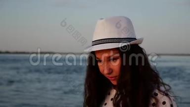 快乐的女孩戴着一顶白色可爱的帽子沿着海边散步，在沙滩上，看着夕阳，微笑着