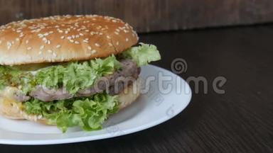 一个大的美味多汁的汉堡，有三层切块、新鲜生菜叶和奶酪，放在一个时髦的白色盘子上