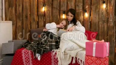 漂亮的年轻妈妈给她可爱的女儿读圣诞故事，她坐在沙发上，裹着毯子