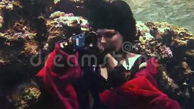 年轻的水下模特自由潜水员穿着红色服装照片相机在红海。