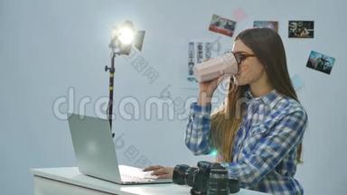 年轻漂亮的女<strong>摄影</strong>师在<strong>办公室里</strong>用手提电脑和喝咖啡
