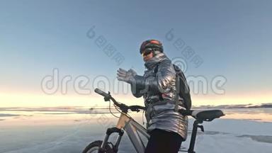 女人在冰上骑自行车。 女孩穿着银色羽绒服，自行车背包和头盔。 女人是