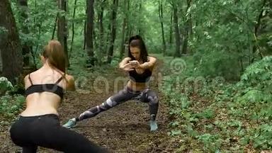 林中两个身材修长的健身少女.. 布鲁内特在路径上练习，他们执行蹲来伸展。