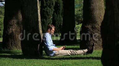 帅哥坐在棕榈树下，用智能手机上网