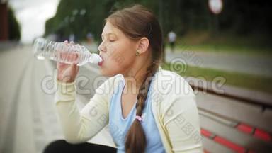 一个小胖女孩在滚筒上喝水。 一个孩子在长凳上的公园里喝水